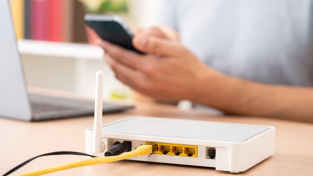 Stock photo showing a Wi-Fi router with a person using a smartphone and computer in background.