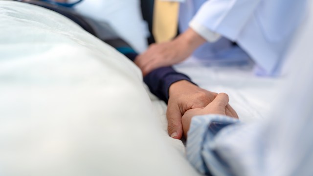 scene of bedridden patient, focus on hand of illness's relative holding hands elderly hopeless senior male with infectious disease, concept of nursing home care or medical treatment in hospital ward